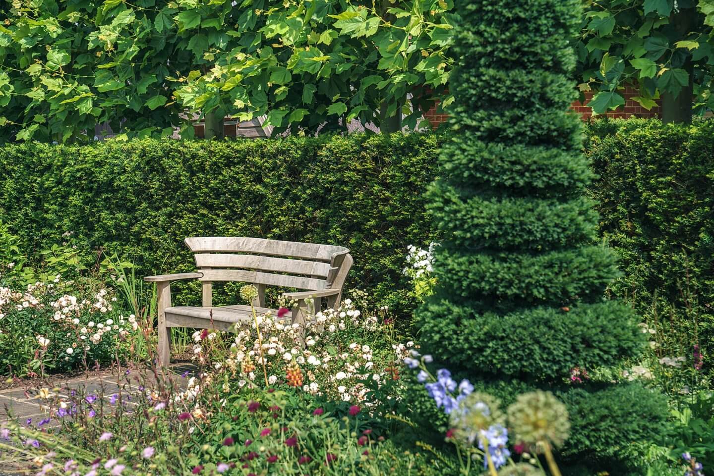 handcrafted steambent oak wooden seating with topiary in a country garden