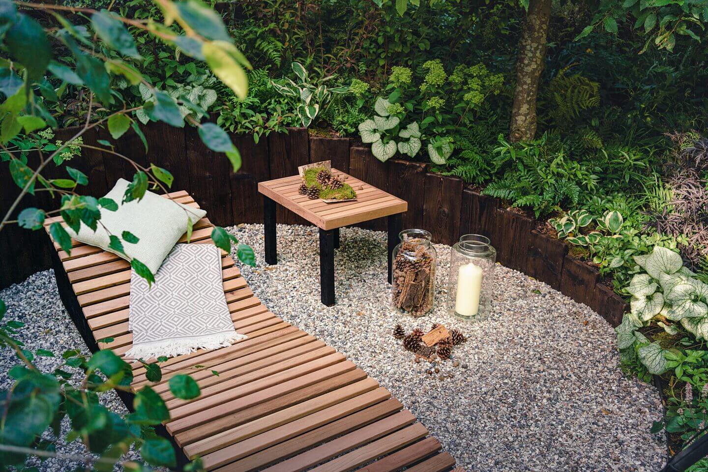 Wooden lounger chair amongst green plants and candles