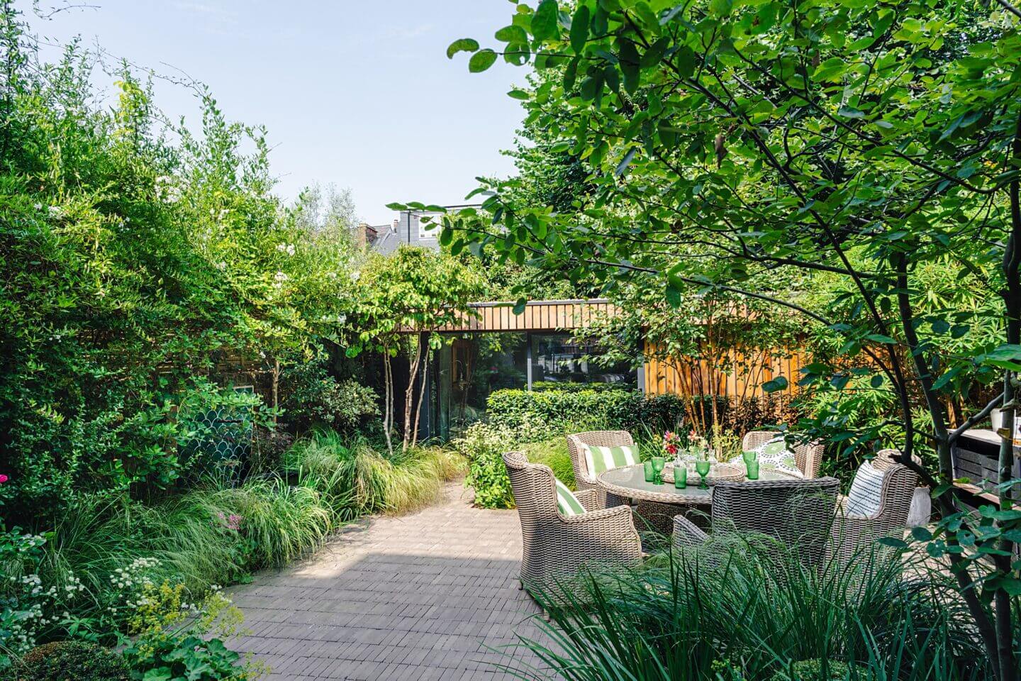 Family garden design urban courtyard with dining area and home office softened by lush green planting London